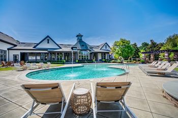 A large swimming pool with two chairs in front of a house.